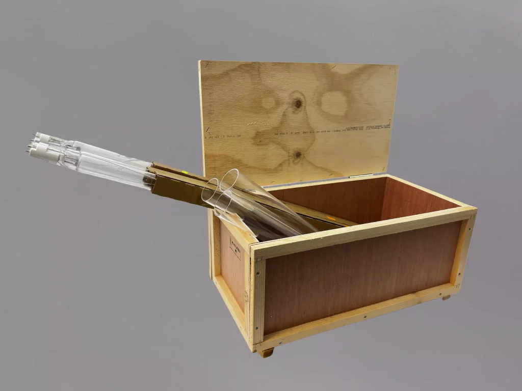 En öppen beredskapslåda i trä som innehåller UV-lampor och kvartsglas, redo för reservdelshantering vid UV-anläggningar.